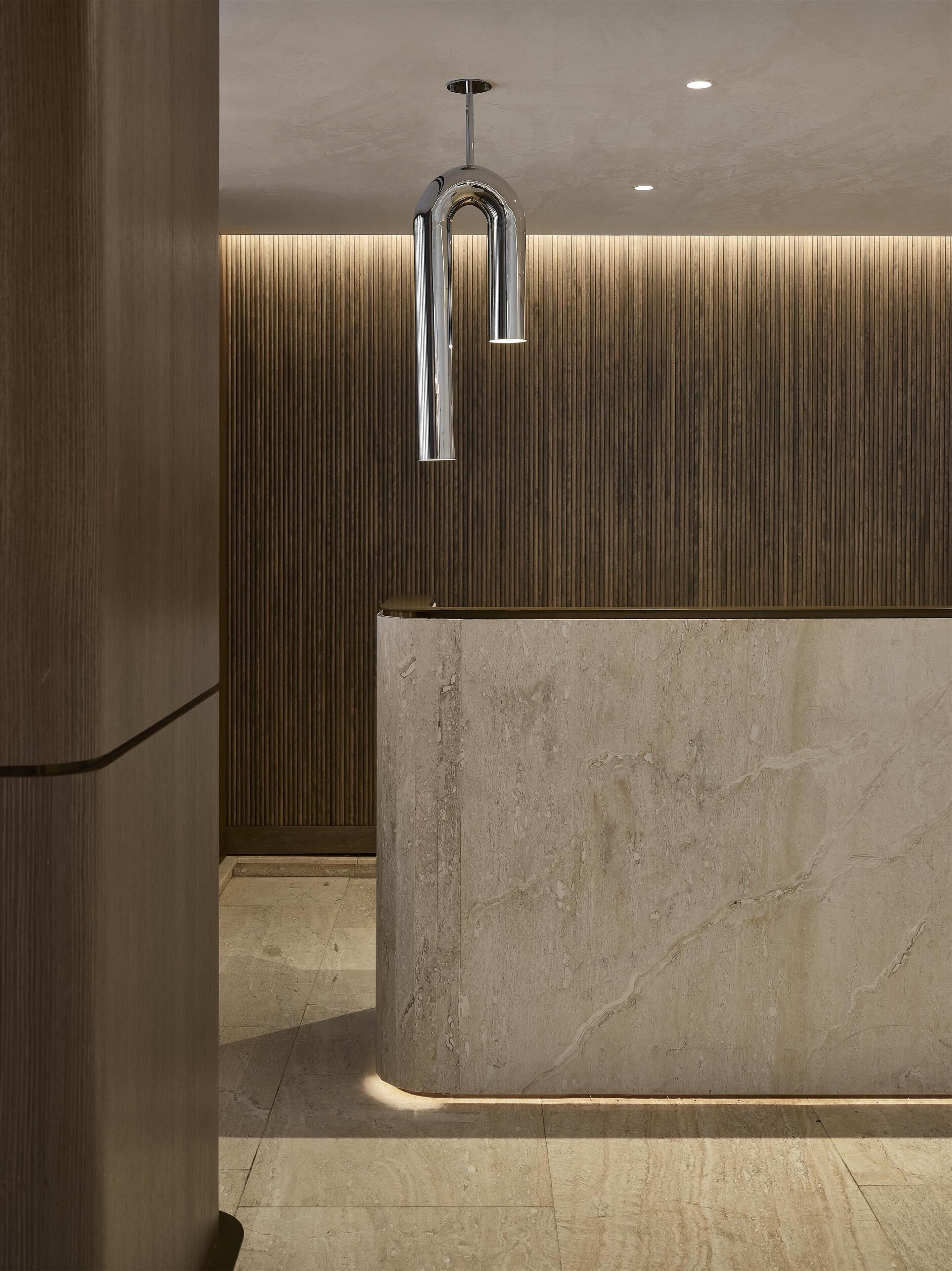 A modern reception area with a marble reception desk, vertical wooden paneling, and a sleek, metallic ceiling light fixture.