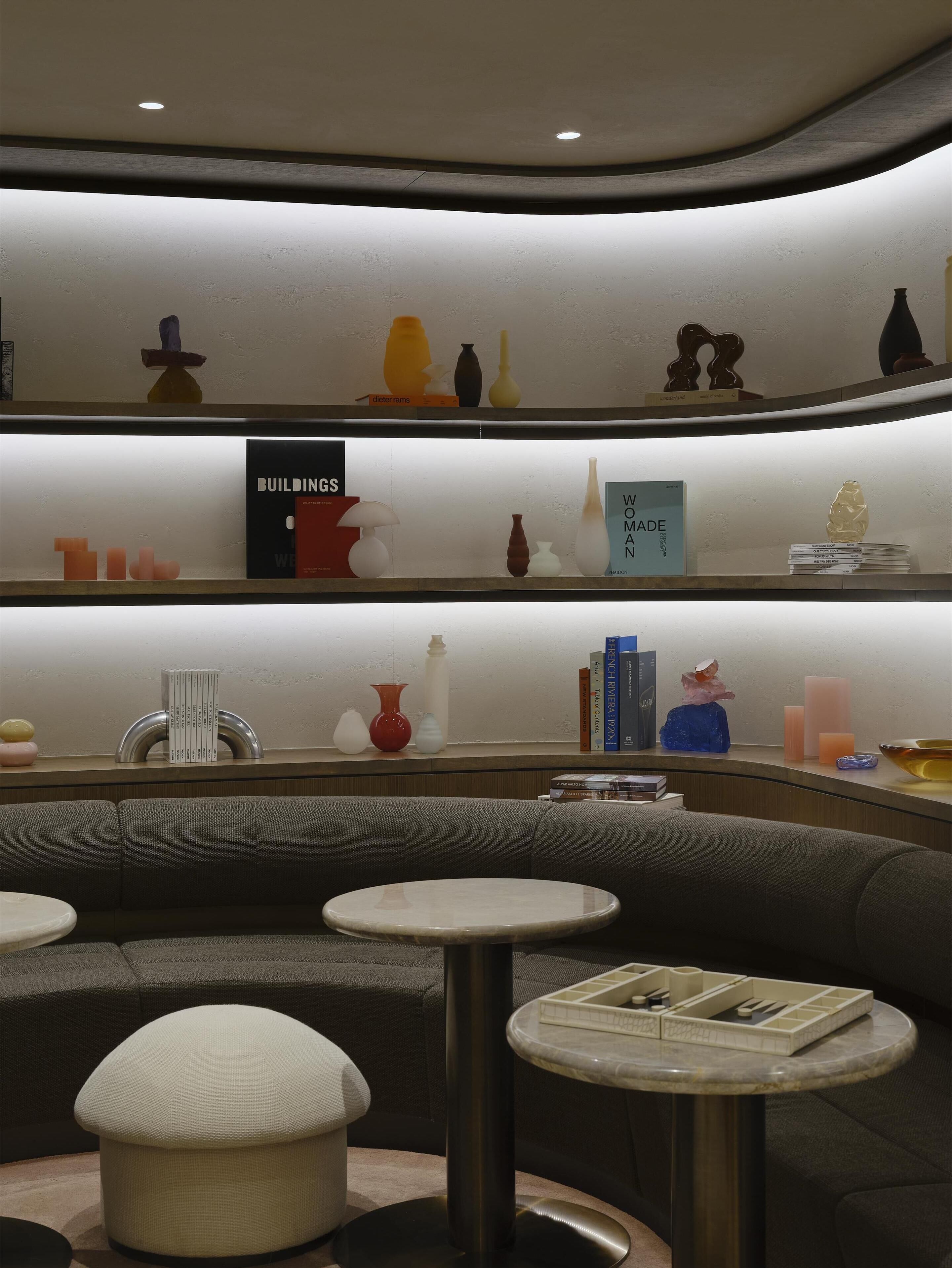 A modern interior with a curved ceiling, a seating area with a sofa and round tables, and shelves with decorative items and books.