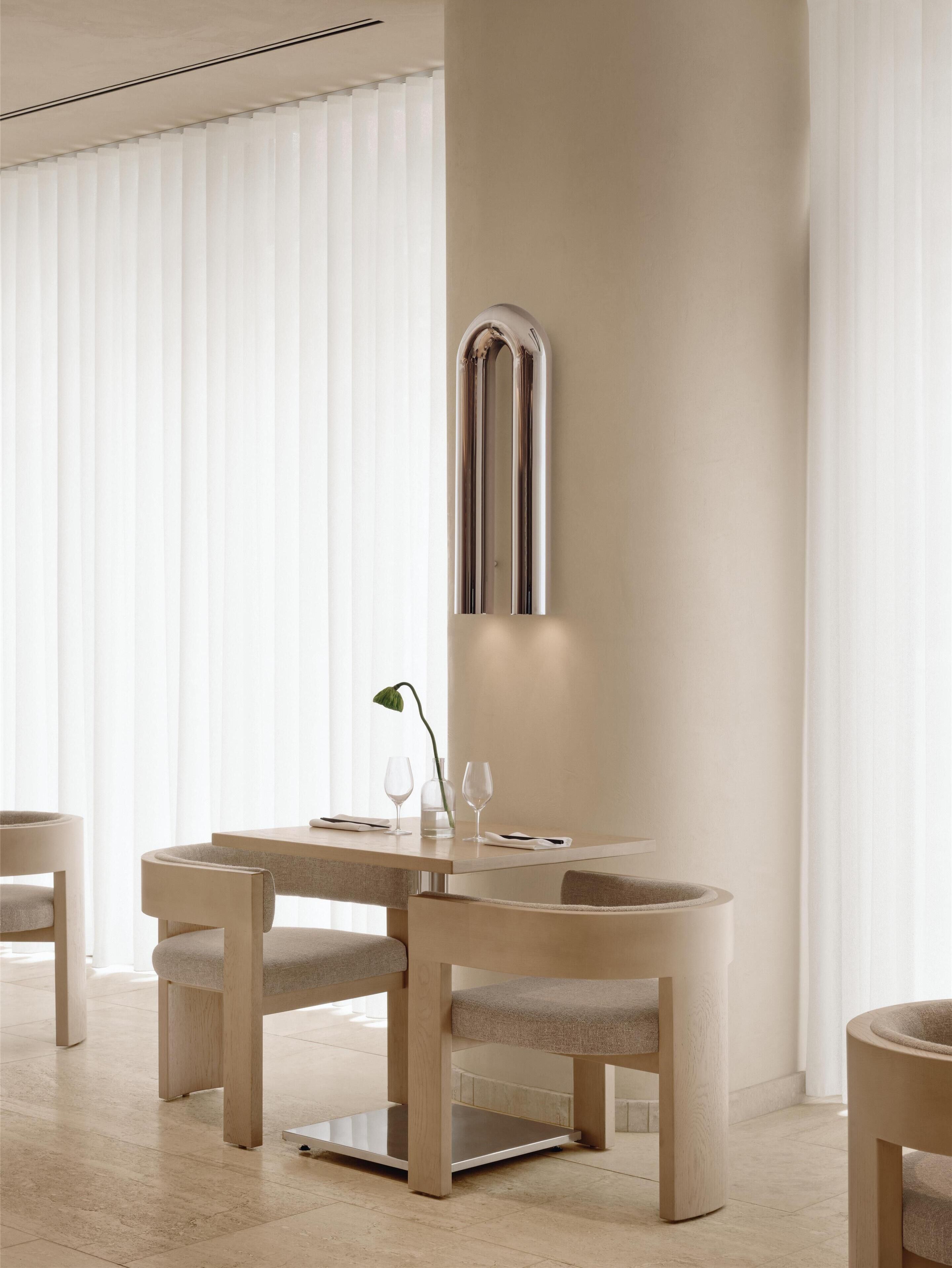 Un comedor moderno con una mesa y sillas minimalistas, un espejo en la pared y un florero con una planta.