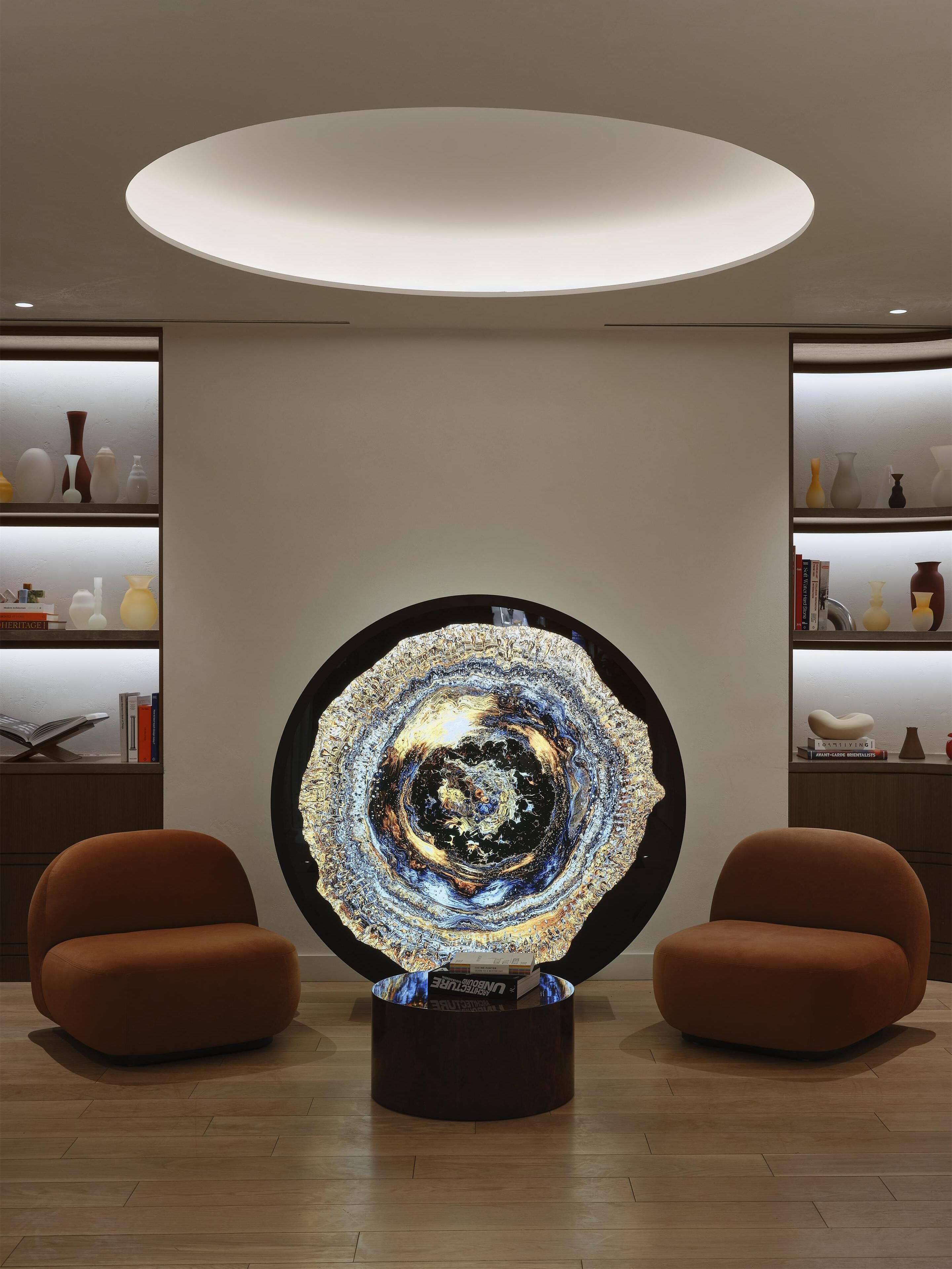 A modern interior with a central art installation, two brown armchairs, and a circular ceiling light.