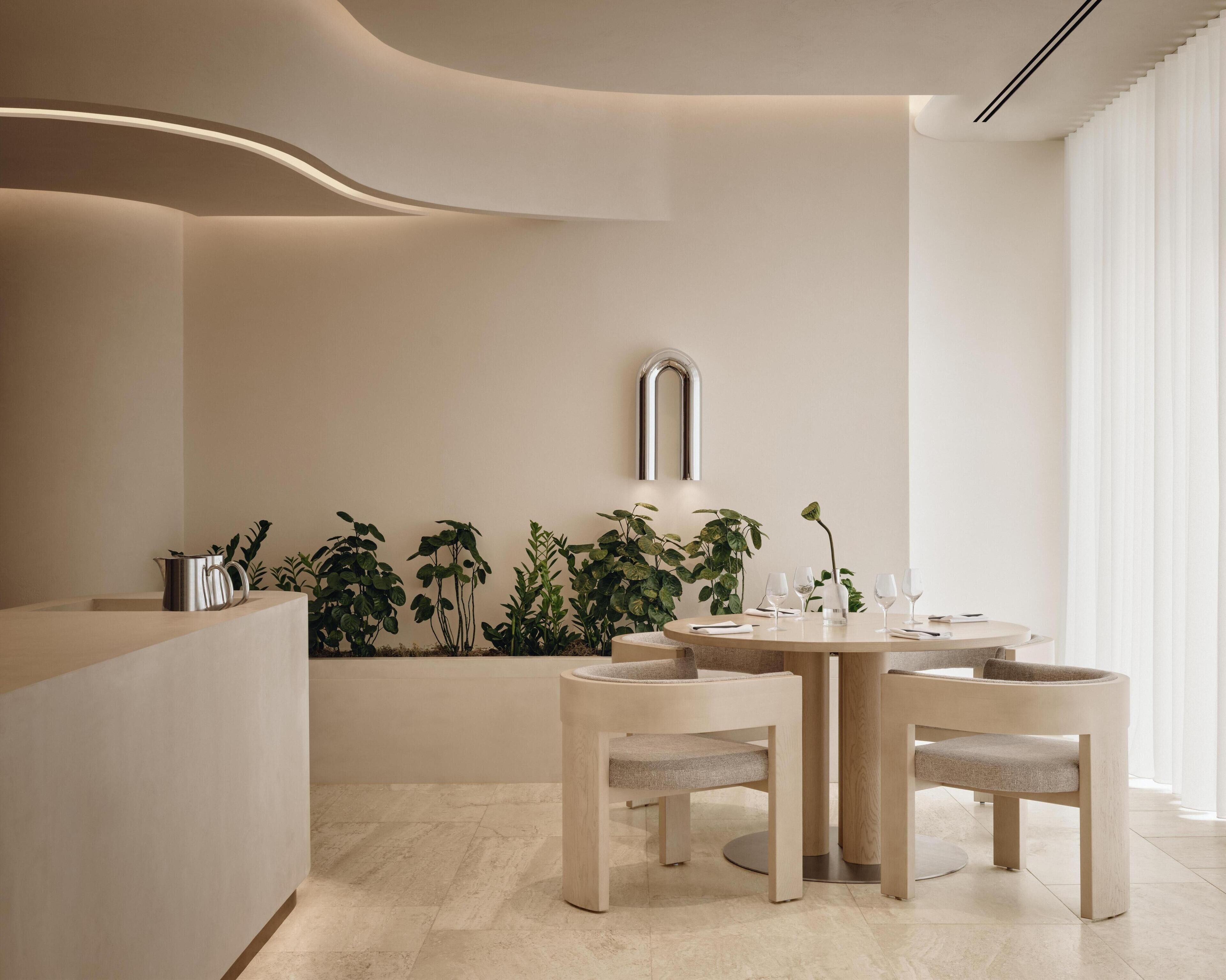 Un coin repas moderne avec une table ronde, deux chaises, une cafetière et une rangée de plantes le long du mur.