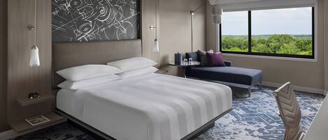 Ein modernes Hotelzimmer mit einem großen Bett, Nachttischen, einem kleinen Schreibtisch und einem Fenster mit Blick auf Grünflächen.