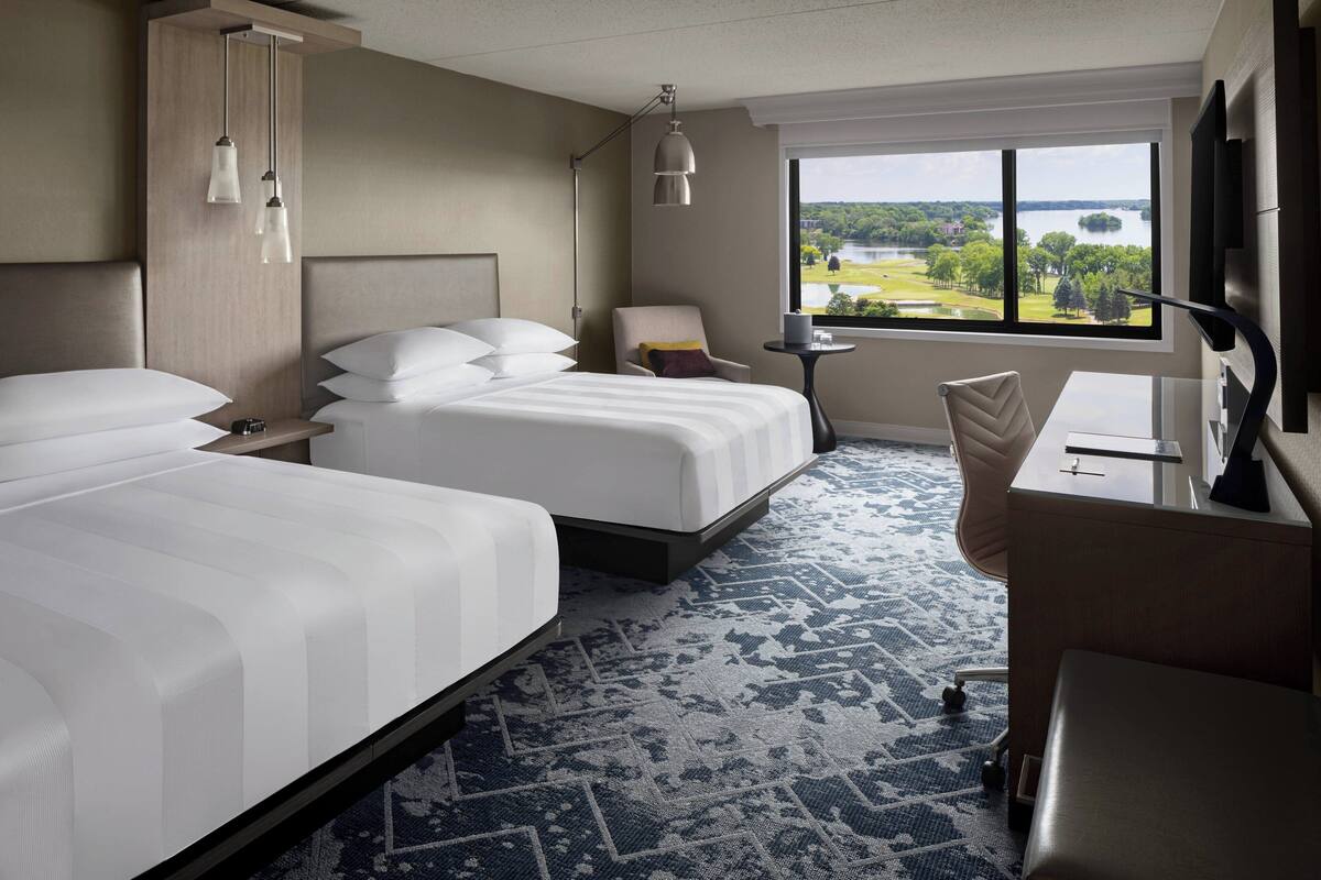 Une chambre d’hôtel avec deux lits, un bureau, une chaise, une petite table et une vue sur un lac.