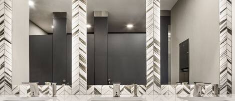 A modern bathroom with a large mirror, two sinks, and a herringbone tile pattern on the walls.