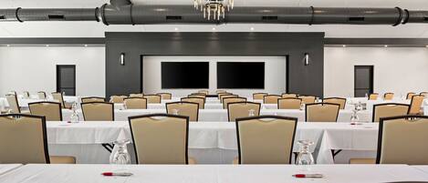 A conference room with multiple tables and chairs, large screens, and a chandelier.