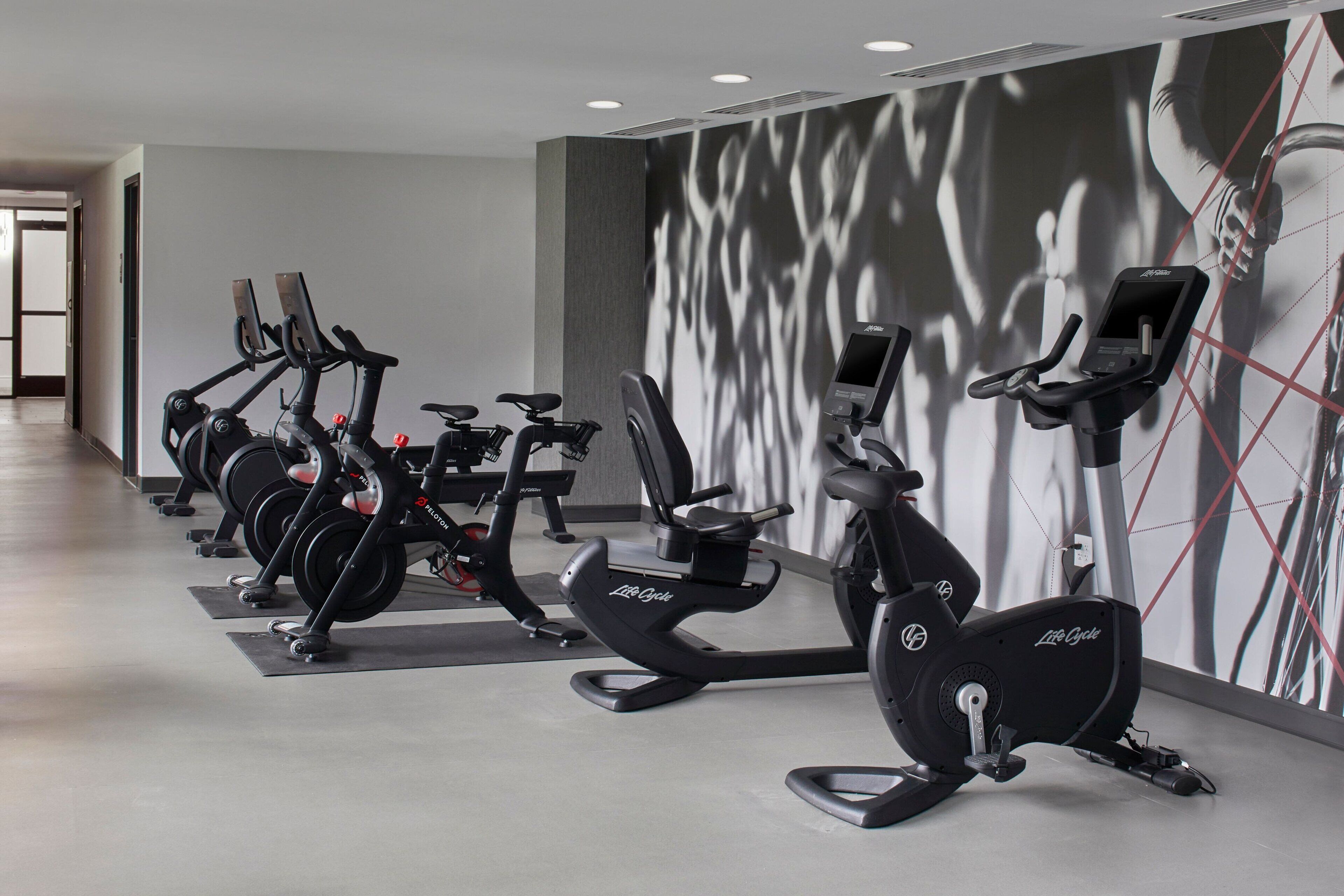 A gym with multiple stationary bikes, a wall-mounted screen, and a door leading to another room.