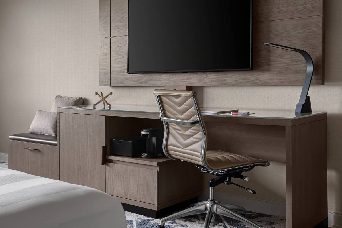 Une chambre d’hôtel équipée d’un lit, d’un bureau avec une chaise, d’un téléviseur à écran plat fixé au mur et d’une machine à café posée sur le bureau.