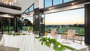 A dining area with a long table set for a meal, large windows offering a view of a golf course, and a modern interior design. - Ann Arbor Marriott Ypsilanti at Eagle Crest (Ypsilanti)