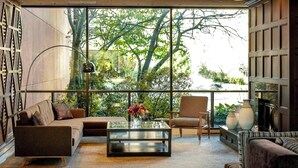 A modern living room with a glass coffee table, sofas, and a large window offering a view of trees and a balcony. - Ann Arbor Marriott Ypsilanti at Eagle Crest (Ypsilanti)