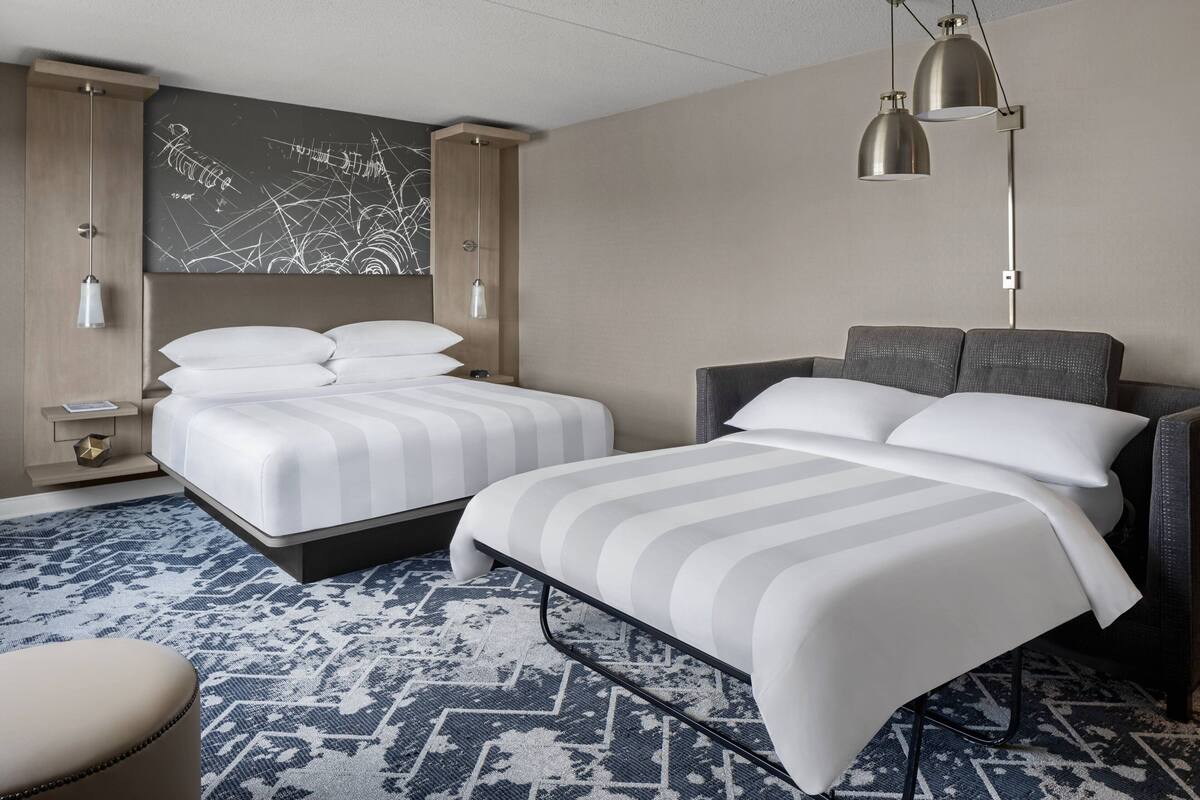 Une chambre d’hôtel avec deux lits, une grande œuvre d’art murale et une moquette à motifs.