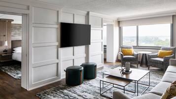 Un salon moderne doté d’un téléviseur à écran plat, d’un canapé, de deux fauteuils, d’une table basse et d’une grande fenêtre offrant une vue dégagée.