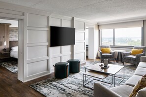 Un salon moderne doté d’un téléviseur à écran plat, d’un canapé, de deux fauteuils, d’une table basse et d’une grande fenêtre offrant une vue dégagée.