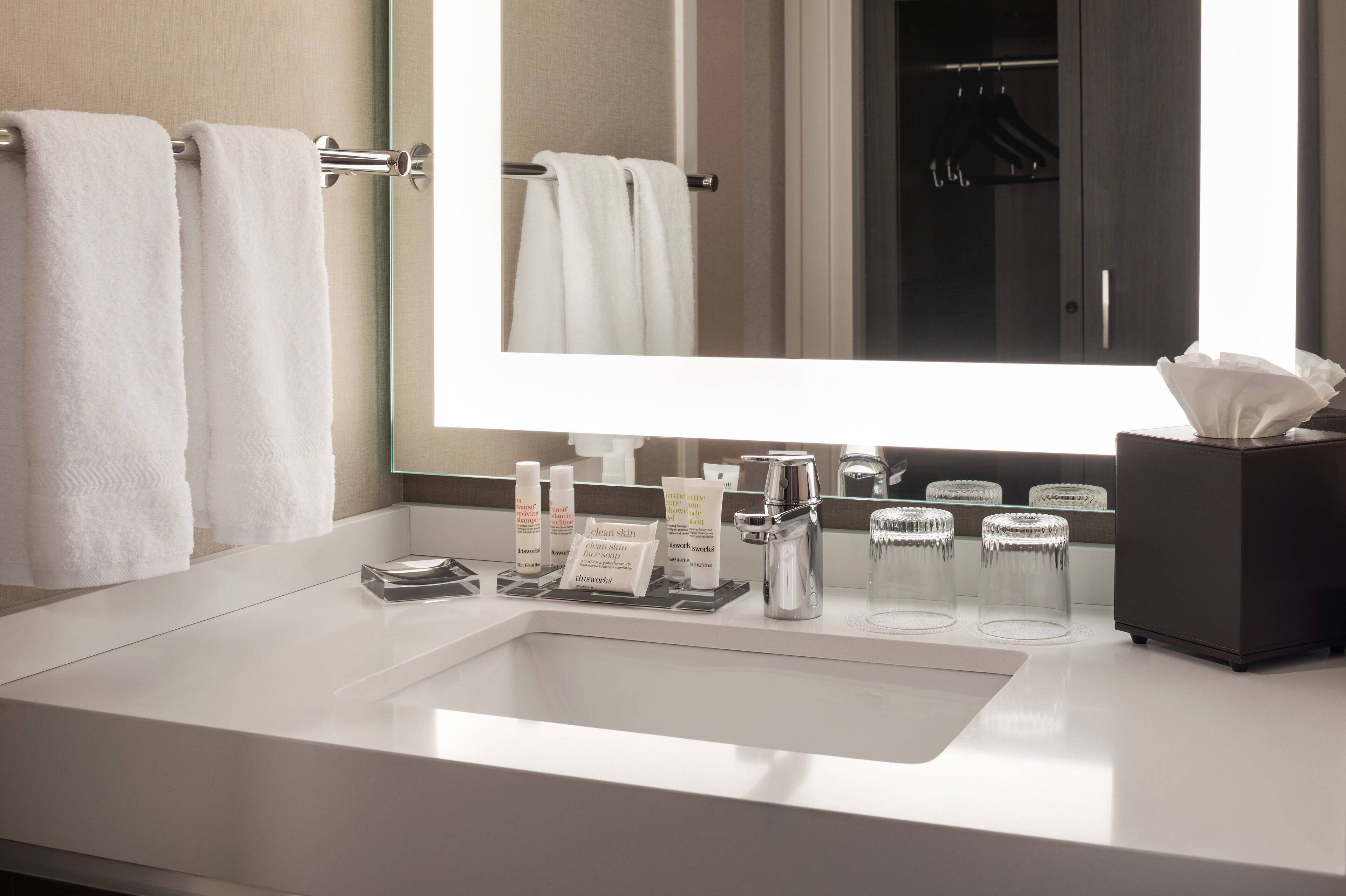 Une salle de bain moderne avec un grand miroir, un lavabo blanc et un porte-serviettes.