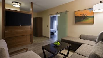 A modern living room with a flat-screen TV, a coffee table with apples, and a painting on the wall.