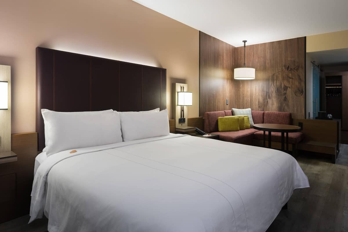 A hotel room with a large bed, a sofa, a small table, and a lamp.