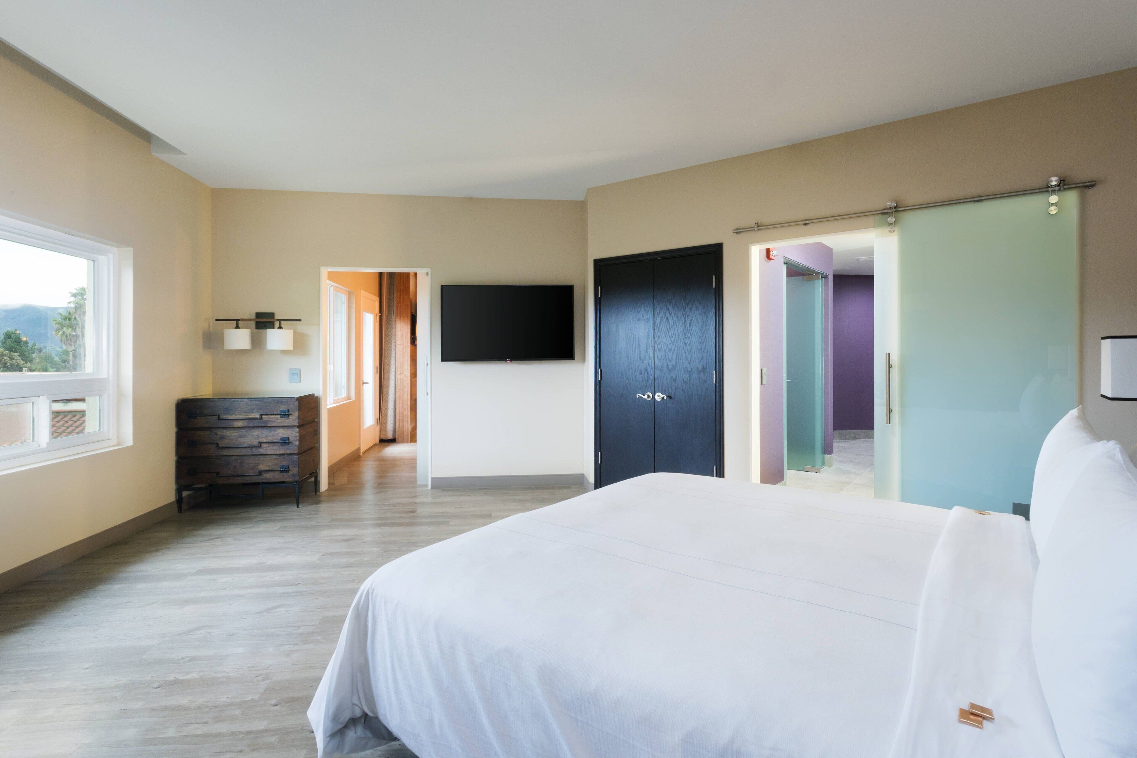 Ein Hotelzimmer mit einem großen Bett, einem flachbildfernseher an der Wand, einem Kleiderschrank und einem Schminktisch.
