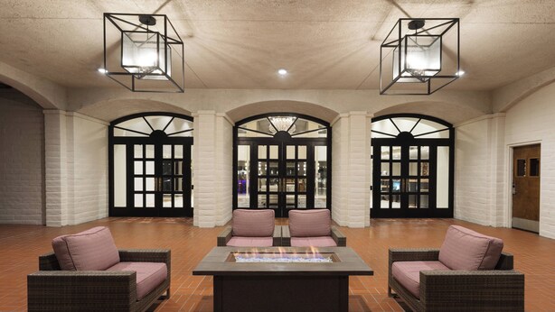 A lobby with a central fire feature, two wicker sofas with cushions, and three arched doorways. - Santa Ynez Valley Marriott (Buellton)