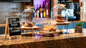 A bakery display with pastries under glass domes, a sign listing items like sausage, egg, and croissant. - Santa Ynez Valley Marriott (Buellton)