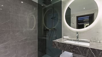 A modern bathroom with a glass-enclosed shower, a marble vanity, and a large mirror with a circular light.