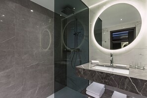 A modern bathroom with a glass-enclosed shower, a marble vanity, and a large mirror with a circular light. - The Westin Grand Berlin (Berlin)