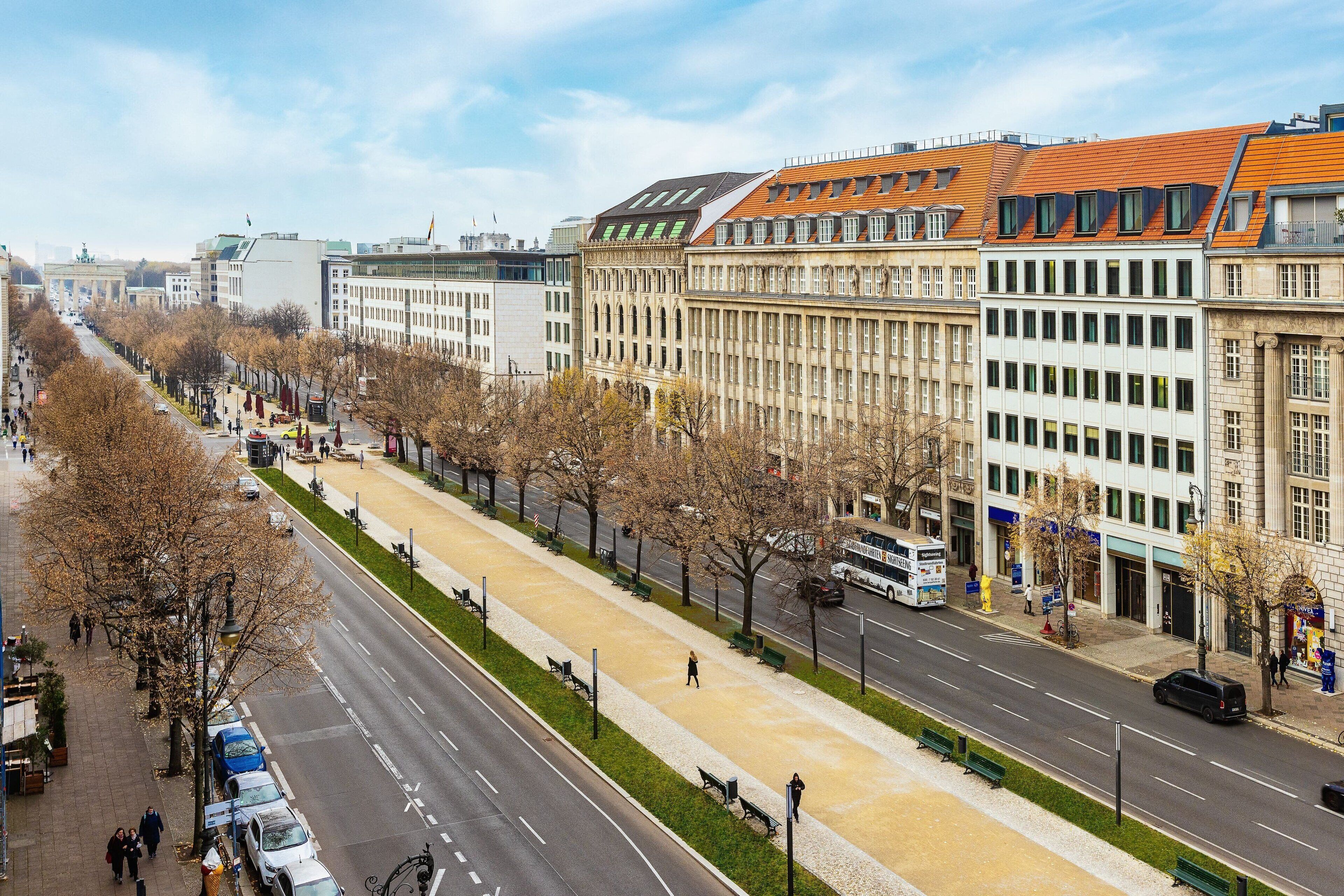 Eine breite Stadtstraße mit Fußgängerweg, gesäumt von Bäumen und Gebäuden.
