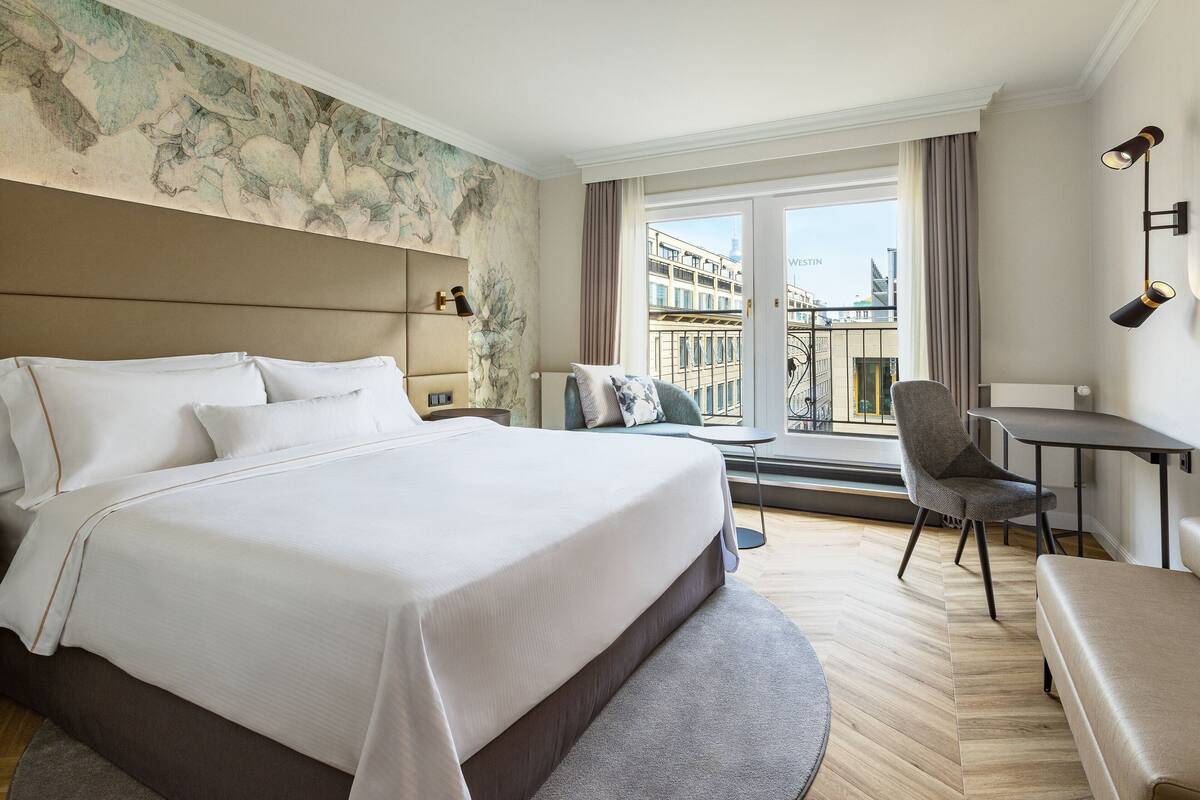 A hotel room with a large bed, a desk, a chair, and a view of the city.