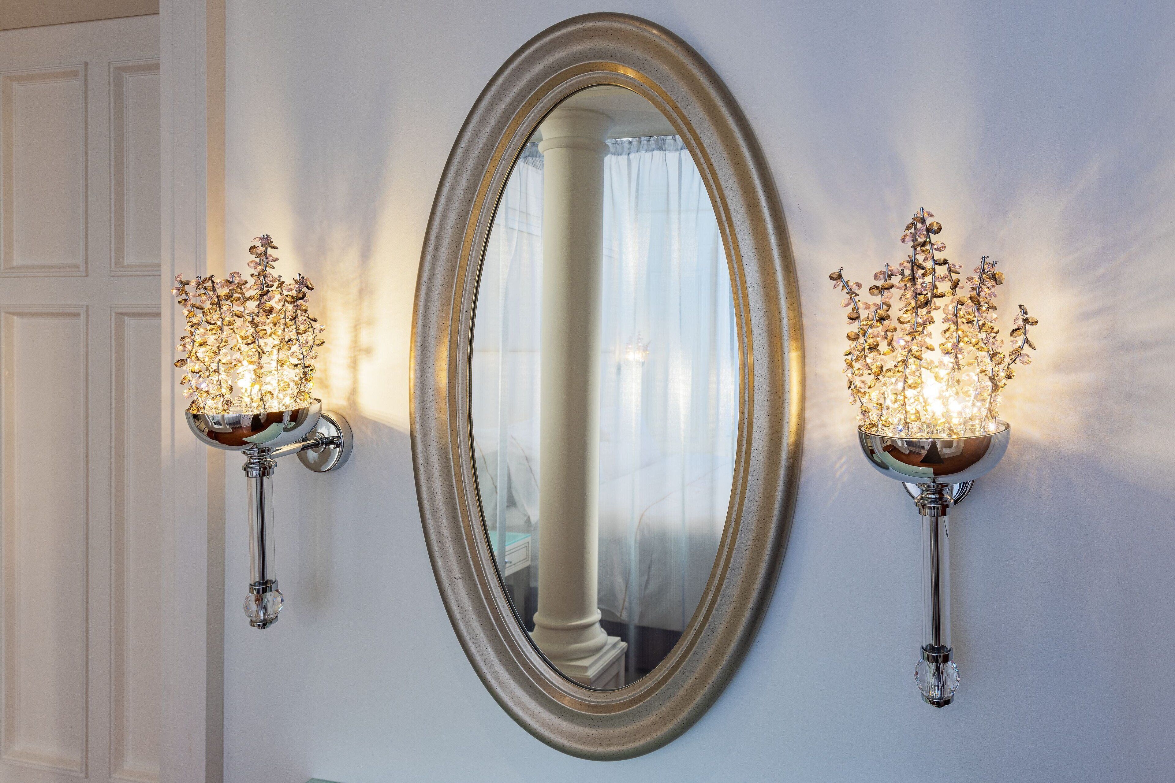 Un espejo con un marco ovalado y dos apliques de pared con candelabros de cristal.