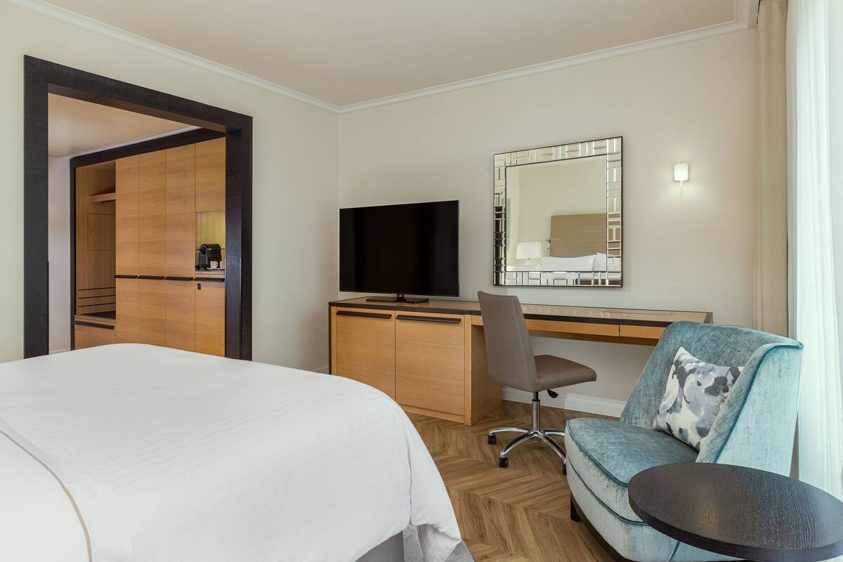 A hotel room with a bed, a desk, a chair, a television, and a mirror.