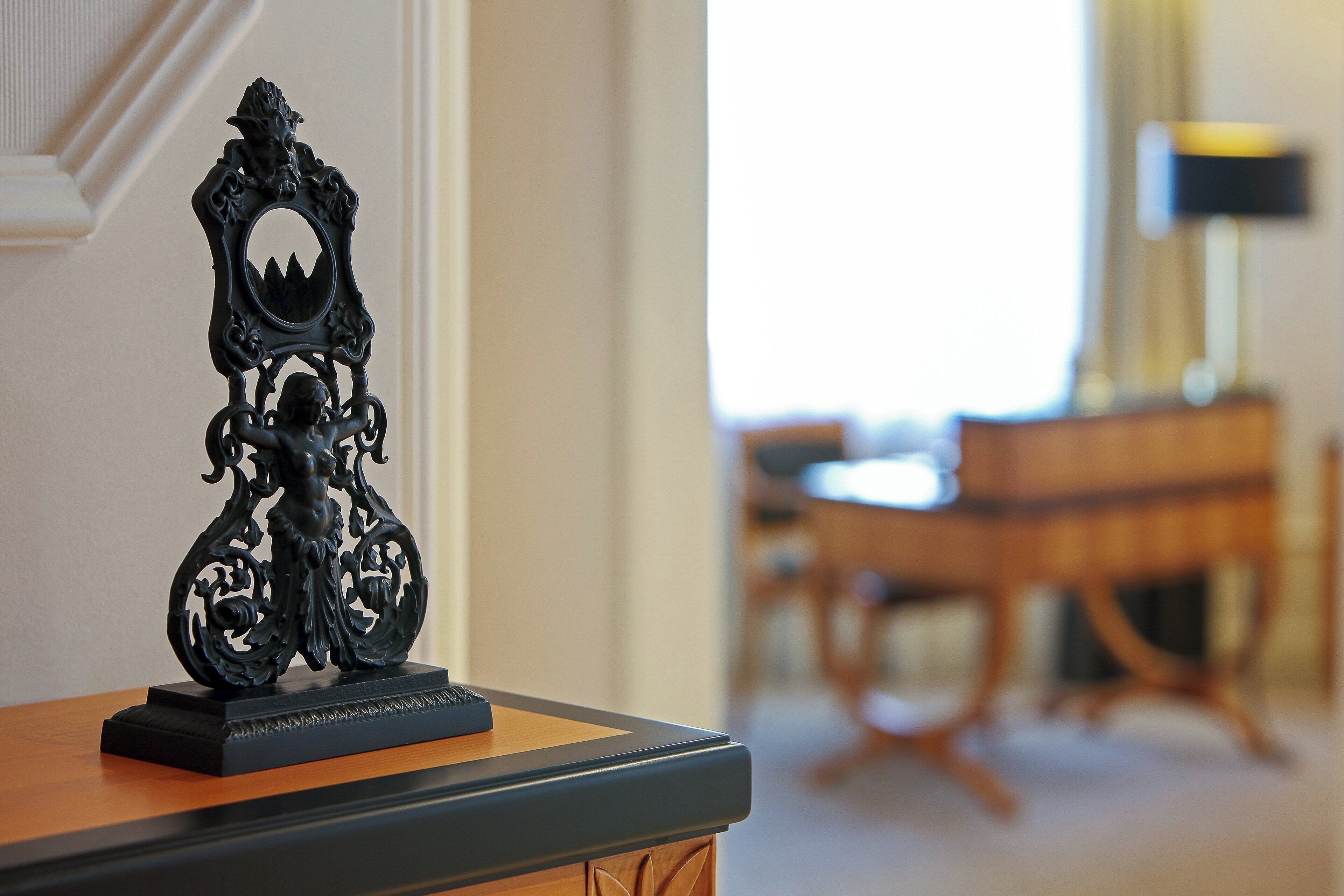 A black ornate sculpture on a wooden table in a room with a dining area in the background.