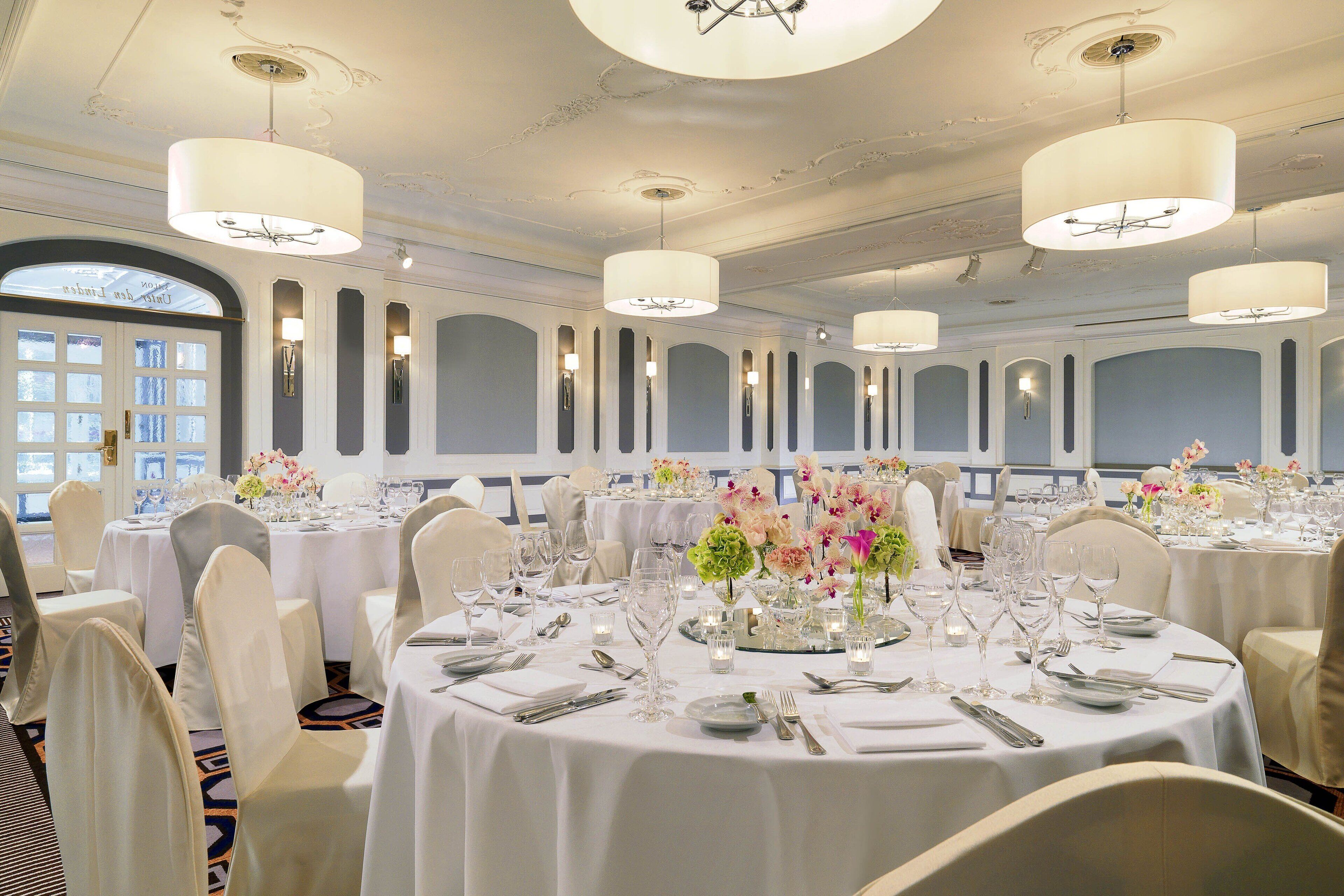 A banquet hall with round tables set for dining, featuring white tablecloths, silverware, and floral centerpieces.