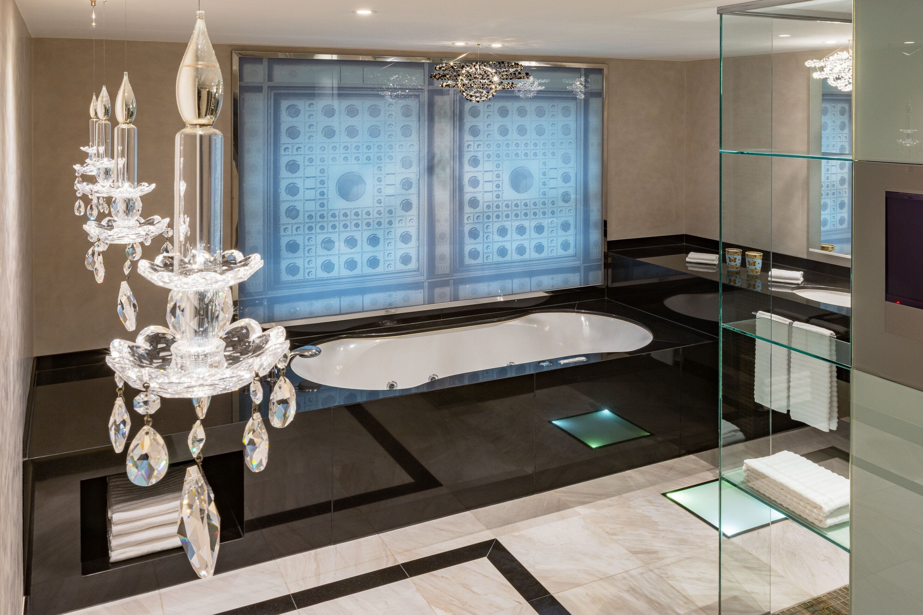 A modern bathroom with a large bathtub, a glass-enclosed shower, and a chandelier.