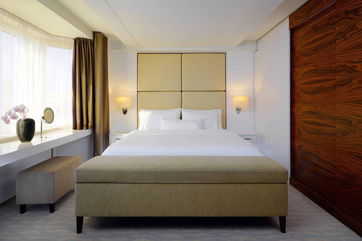 A modern hotel room with a large bed, bedside lamps, a window with curtains, and a wooden accent wall.