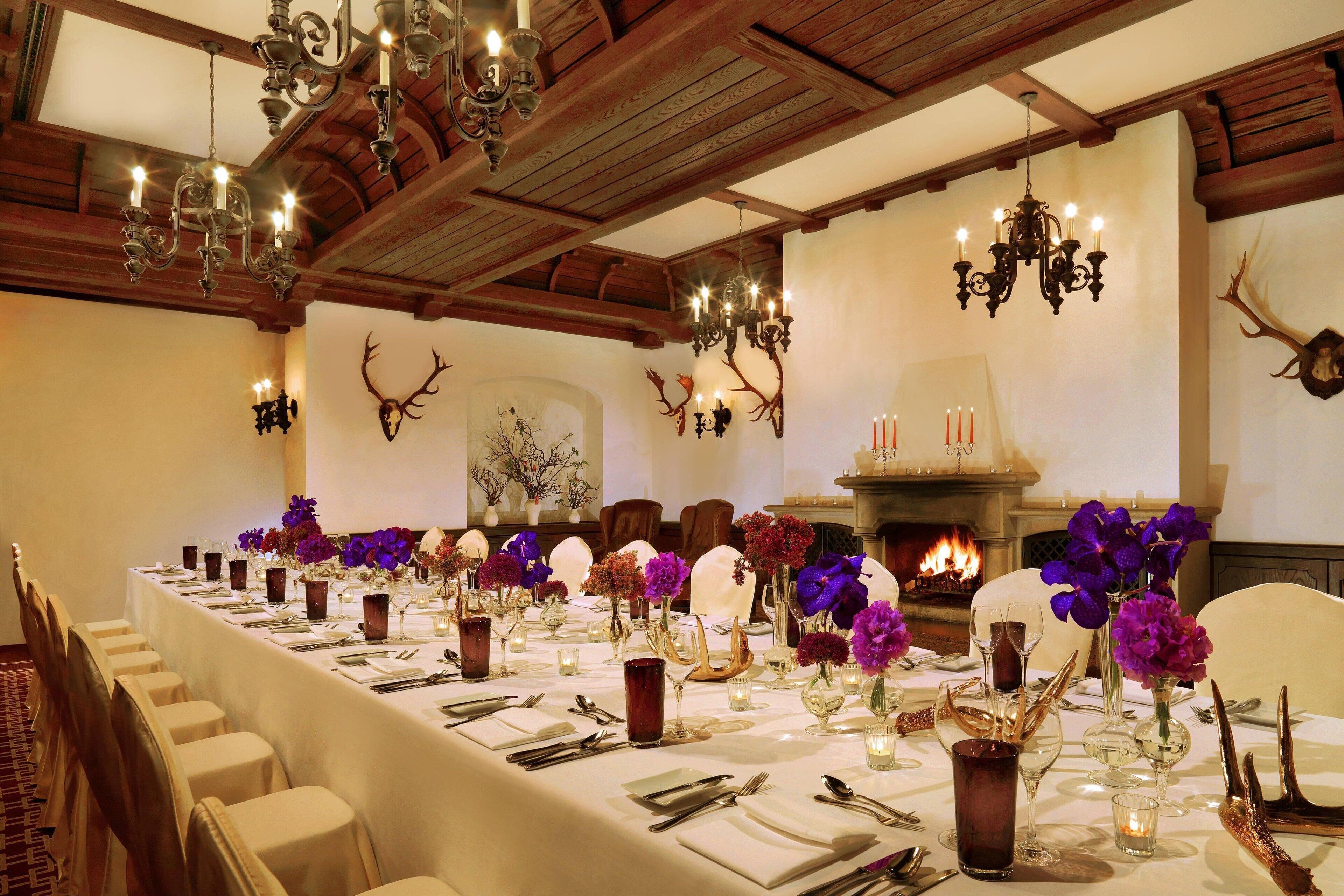 A long dining table set for a formal meal, with chandeliers and antlers on the walls.