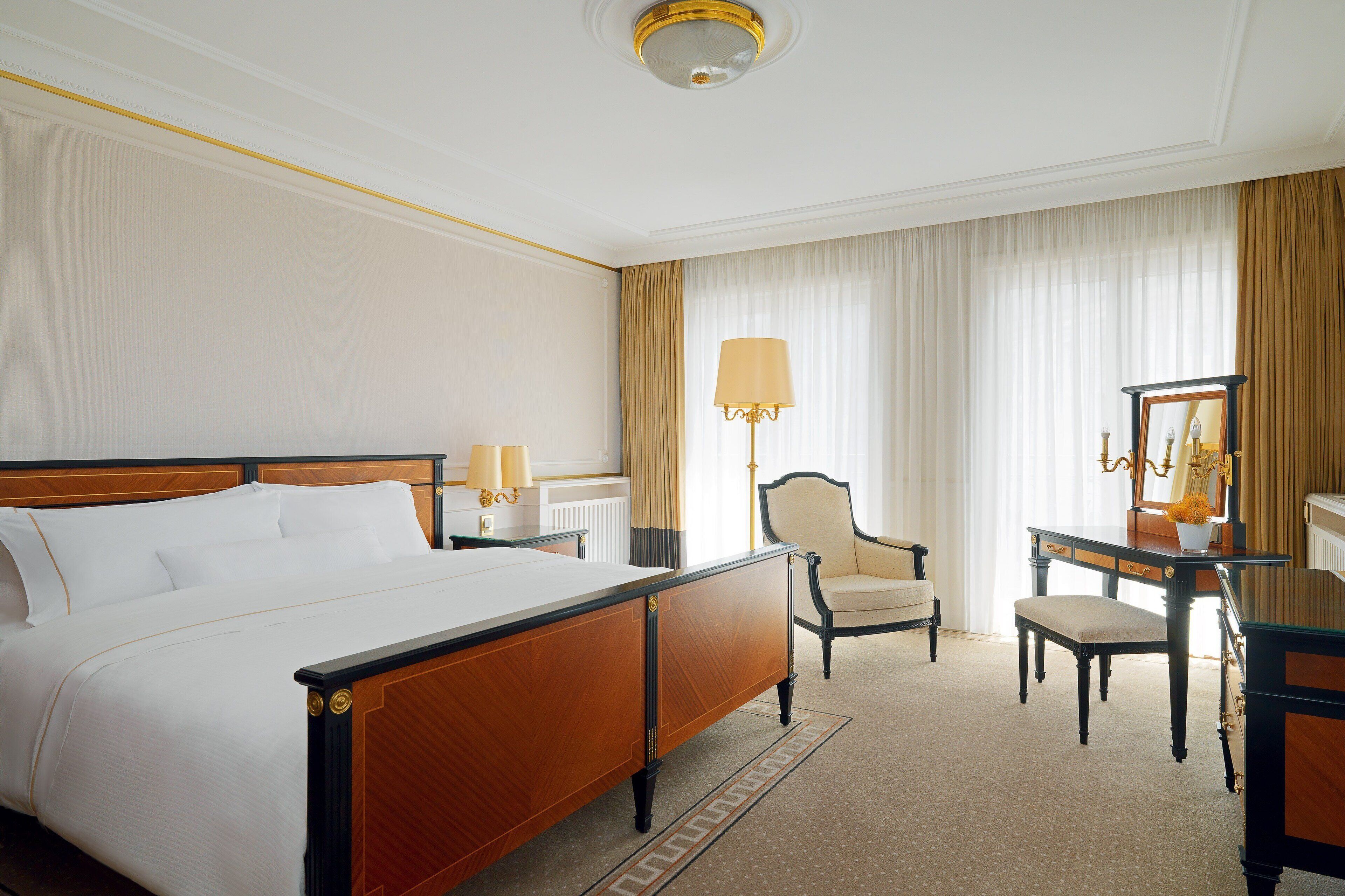 Quarto de hotel com uma cama grande, uma escrivaninha, uma cadeira, um abajur e um espelho.