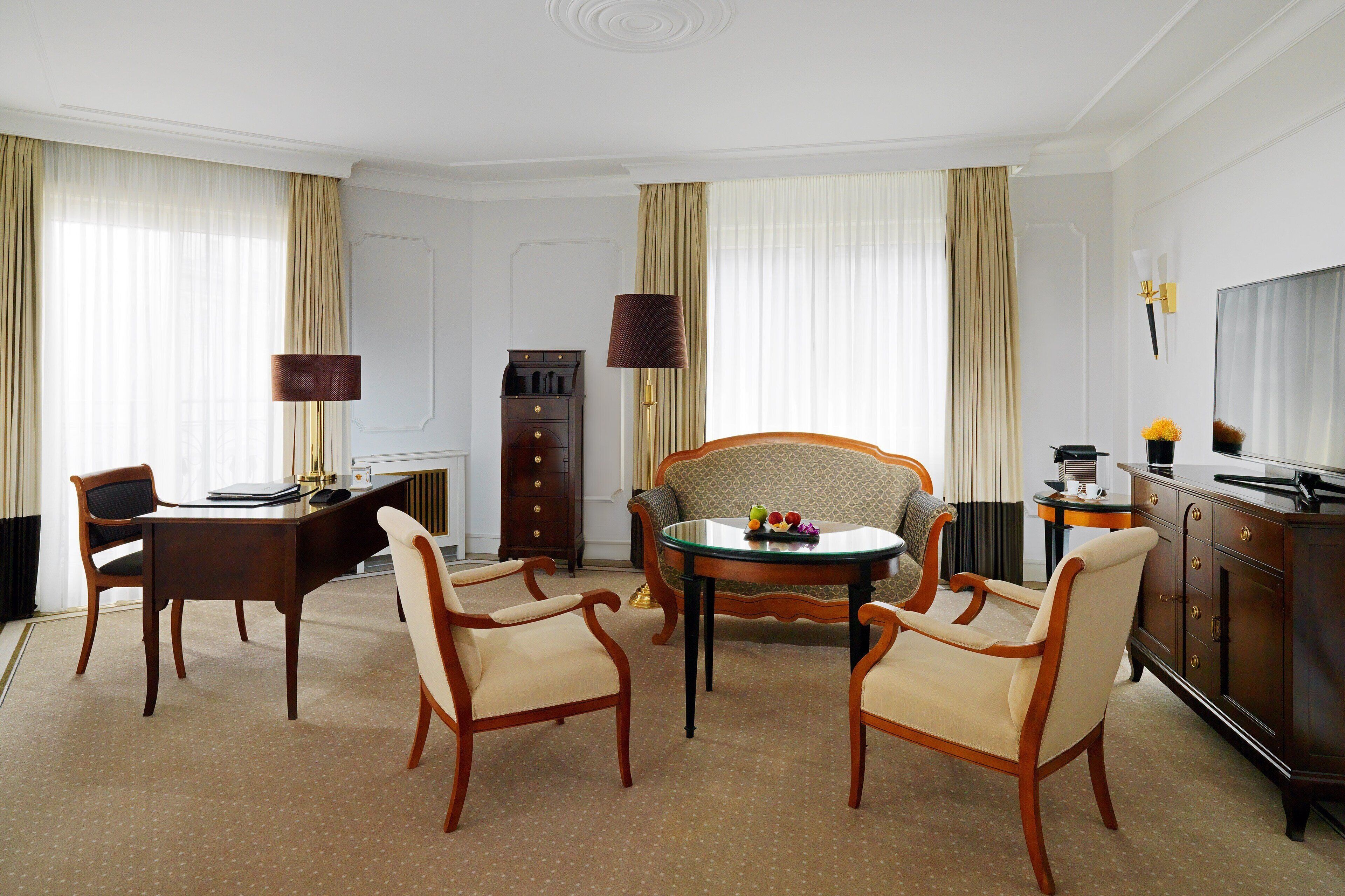 A hotel room with a dining table, two chairs, a sofa, a TV, a lamp, and a cabinet.