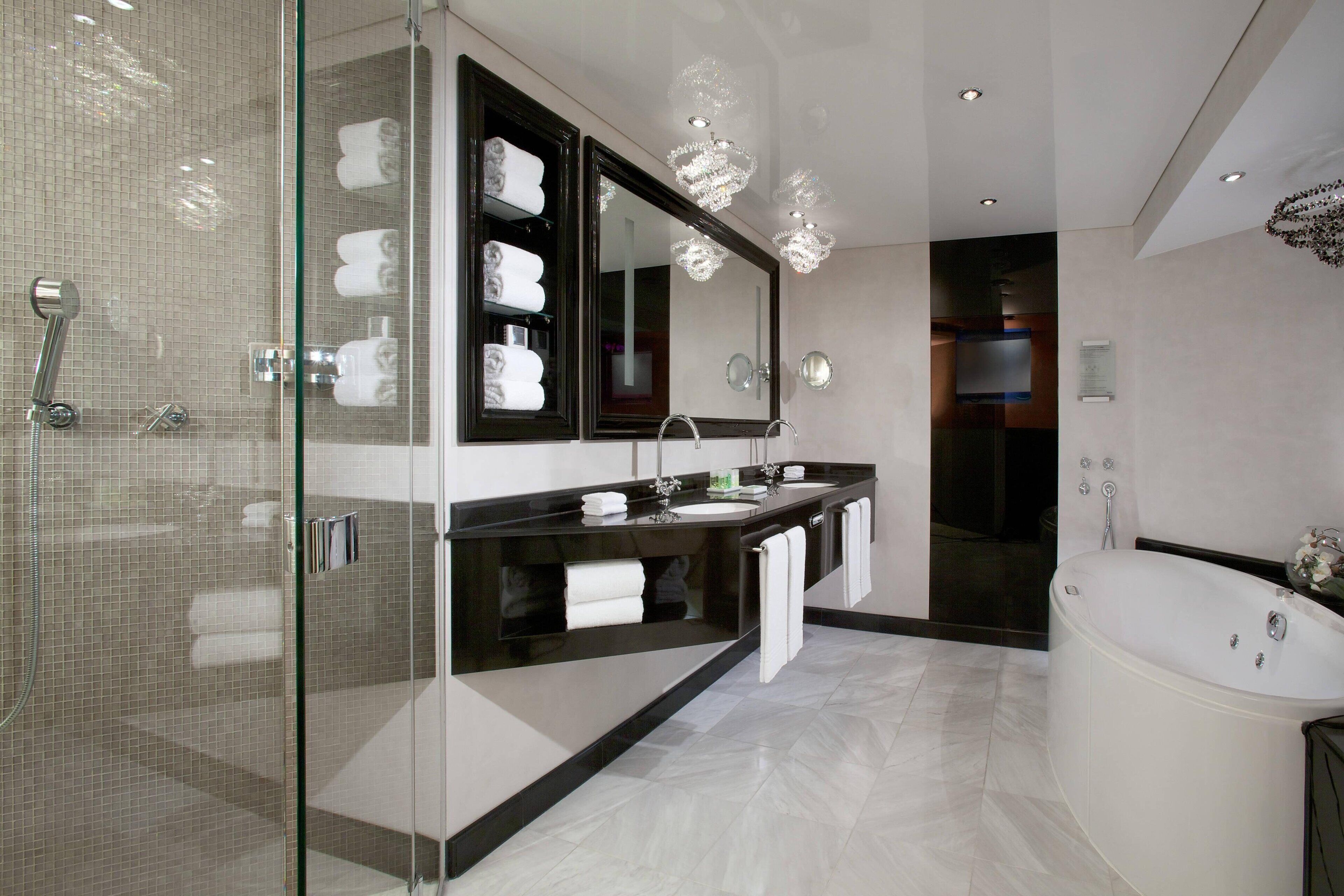 A modern bathroom with a glass shower enclosure, a large mirror, a freestanding bathtub, and a vanity with a dark countertop.