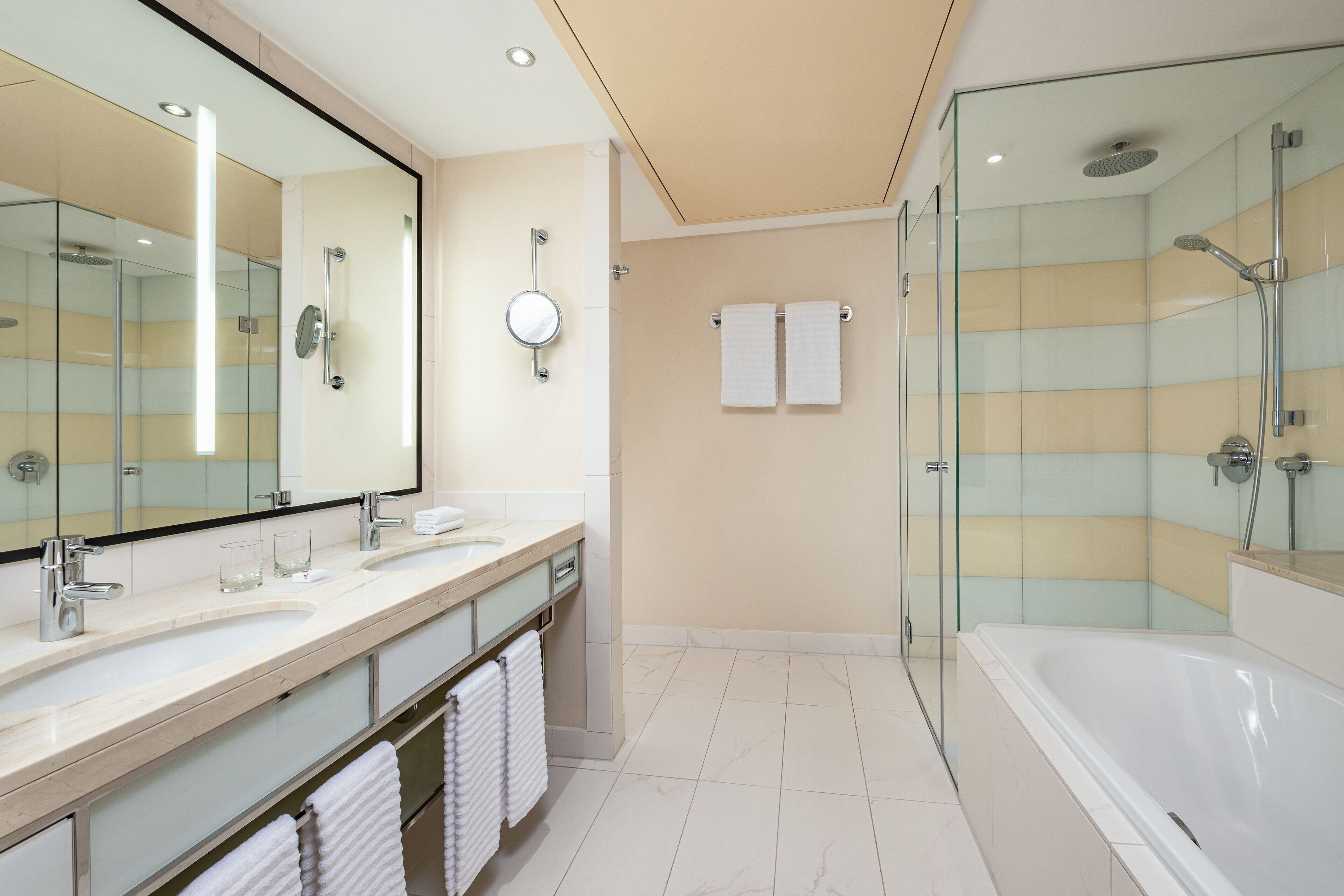 A modern bathroom with a glass-enclosed shower, a large mirror, and a bathtub.