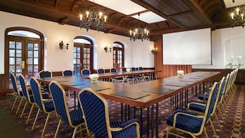 A conference room with a long table, blue chairs, chandeliers, and arched windows.