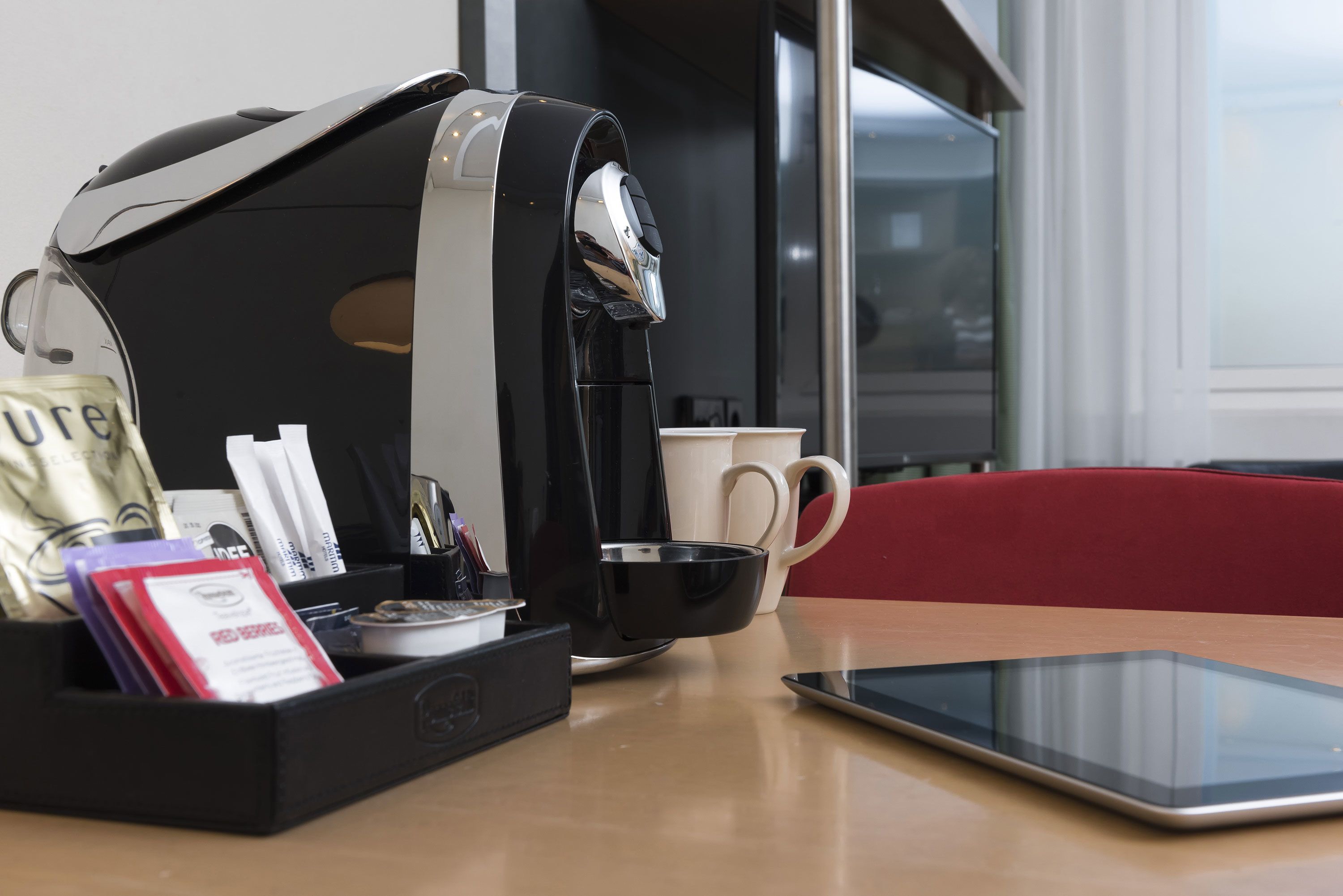 A coffee machine, a tablet, a mug, and a bag of coffee on a table.
