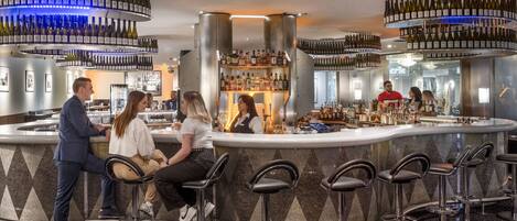 Zona de bar con diferentes distribuciones de mesas y una variedad de botellas expuestas en estanterías.