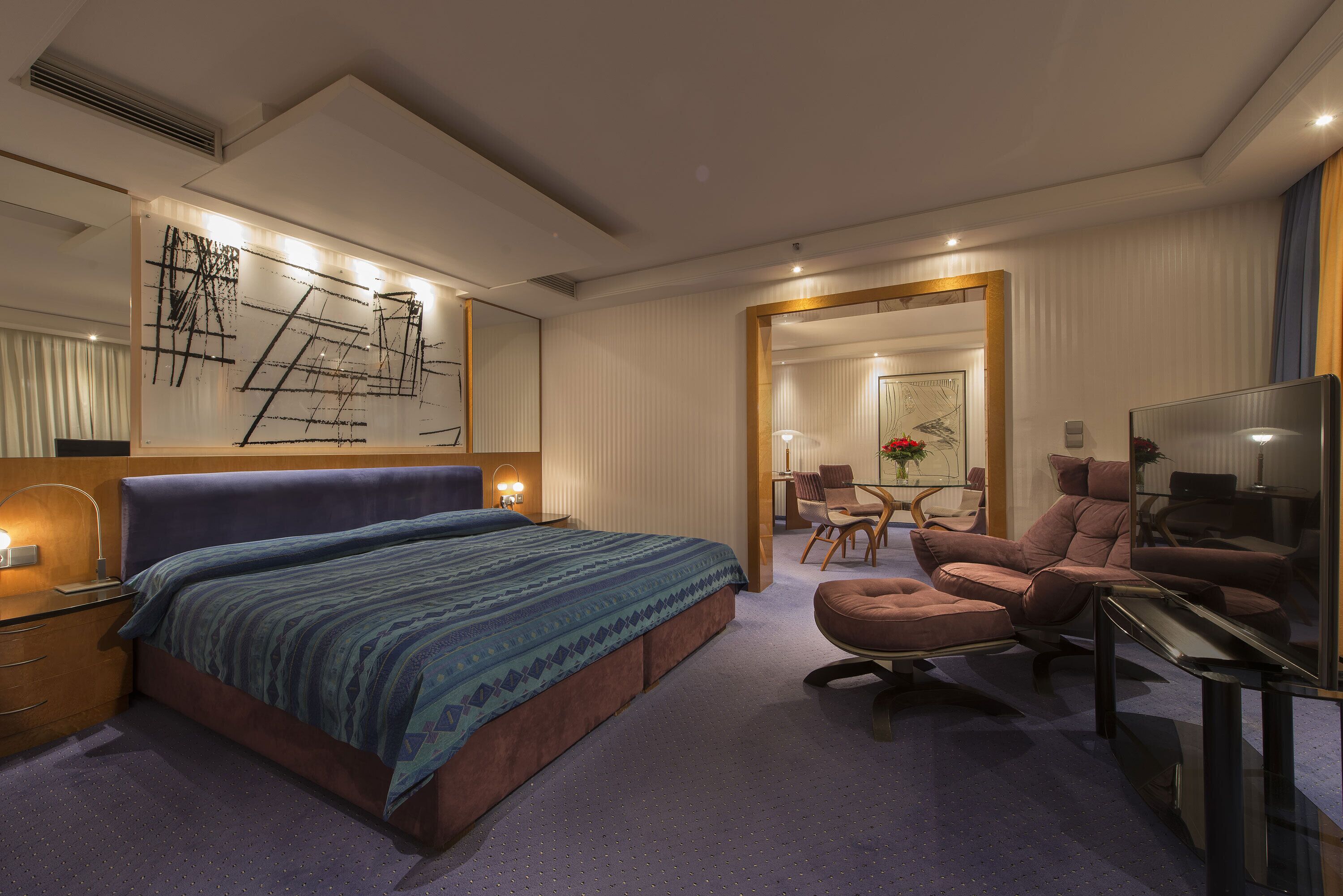 Una habitación de hotel moderna con una cama grande, un espacio de descanso con sofá y sillones, un escritorio y un espejo amplio.