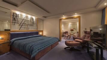 Una habitación de hotel moderna con una cama grande, un espacio de descanso con sofá y sillones, un escritorio y un espejo amplio.