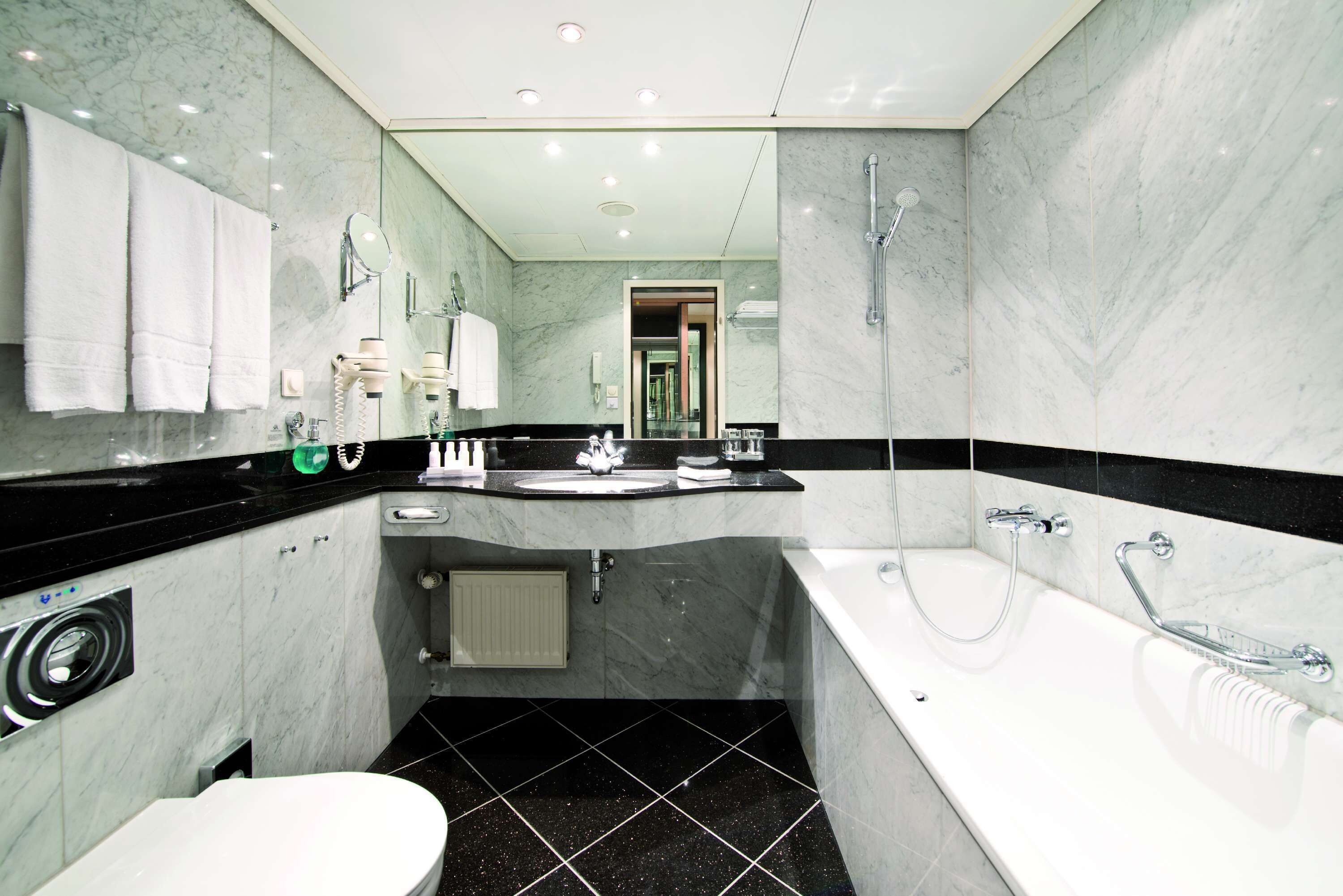 A modern bathroom with a large mirror, a bathtub, a toilet, and a sink.