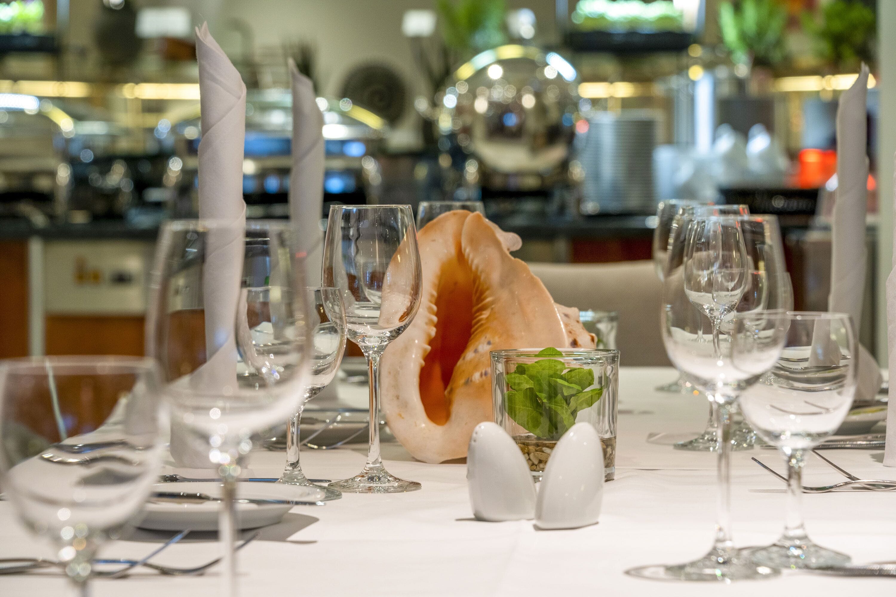A dining table set with wine glasses, plates, and a decorative shell centerpiece.