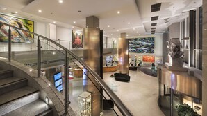 Un moderno vestíbulo de hotel con una escalera de cristal, una recepción y obras de arte en las paredes.