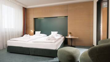 A modern hotel room with a large bed, a small table, and a green armchair.