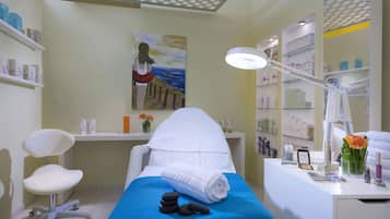 A clean, well-lit room with a massage table, a chair, a desk with shelves of products, and a painting on the wall.