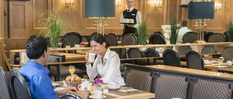 A hotel dining area with wooden paneling, multiple tables, and chairs.