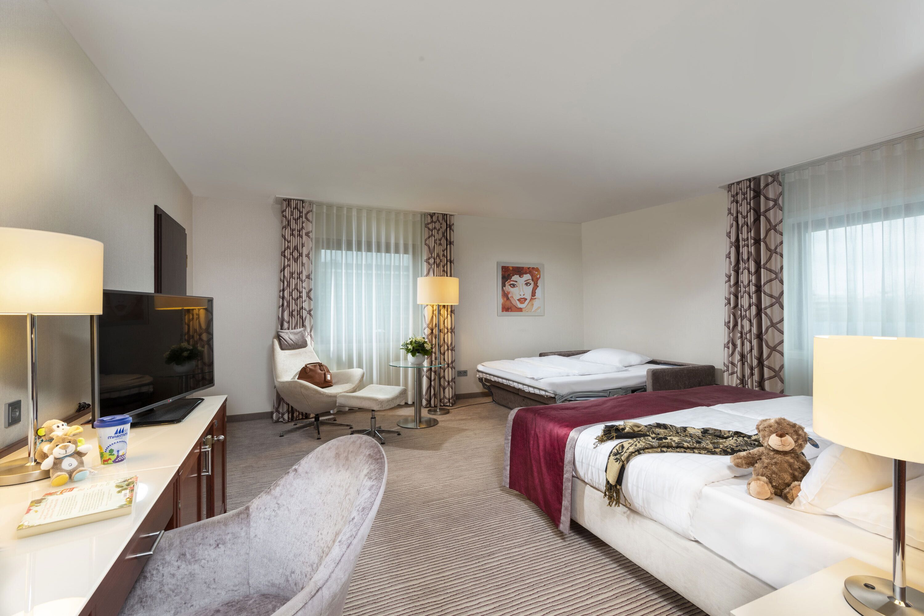 Una habitación de hotel con una cama, un escritorio con televisor, una silla, una mesita de noche y una lámpara.