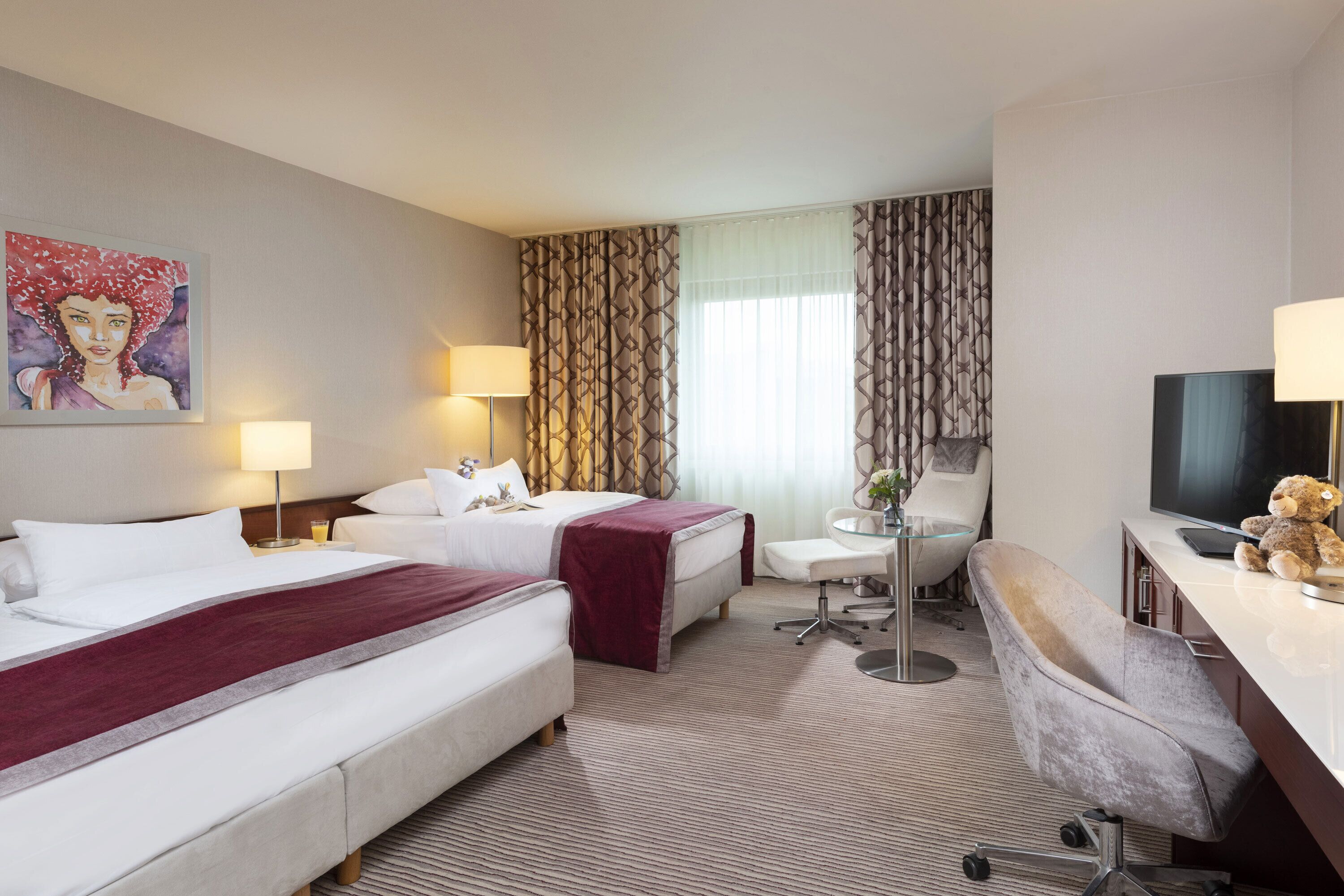 A hotel room with two beds, a desk, a chair, a TV, and a painting on the wall.